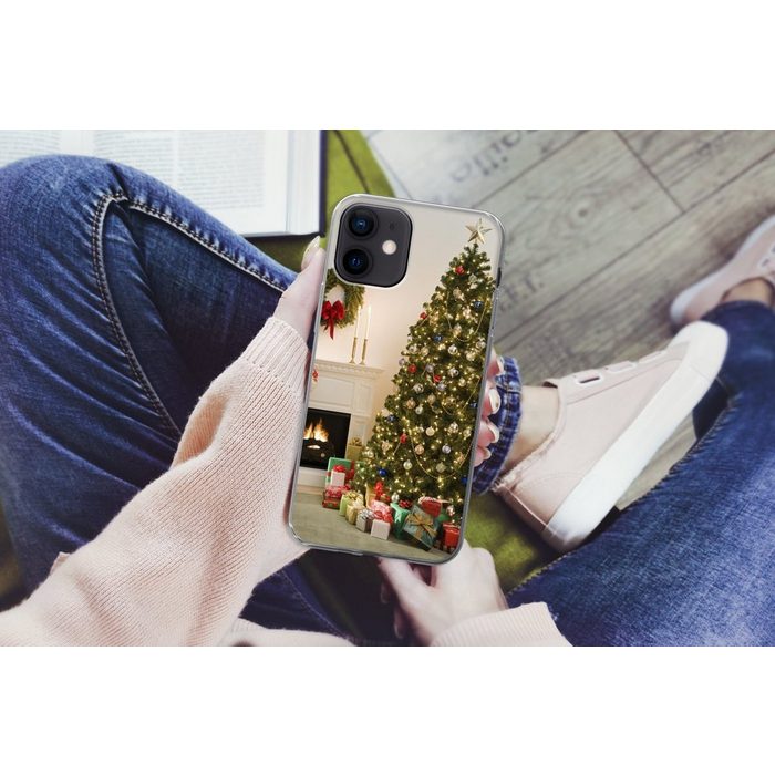 MuchoWow Handyhülle Ein Weihnachtsbaum mit Geschenken neben einem Kamin Handyhülle Apple iPhone 12 Smartphone-Bumper Print Handy ZV11090