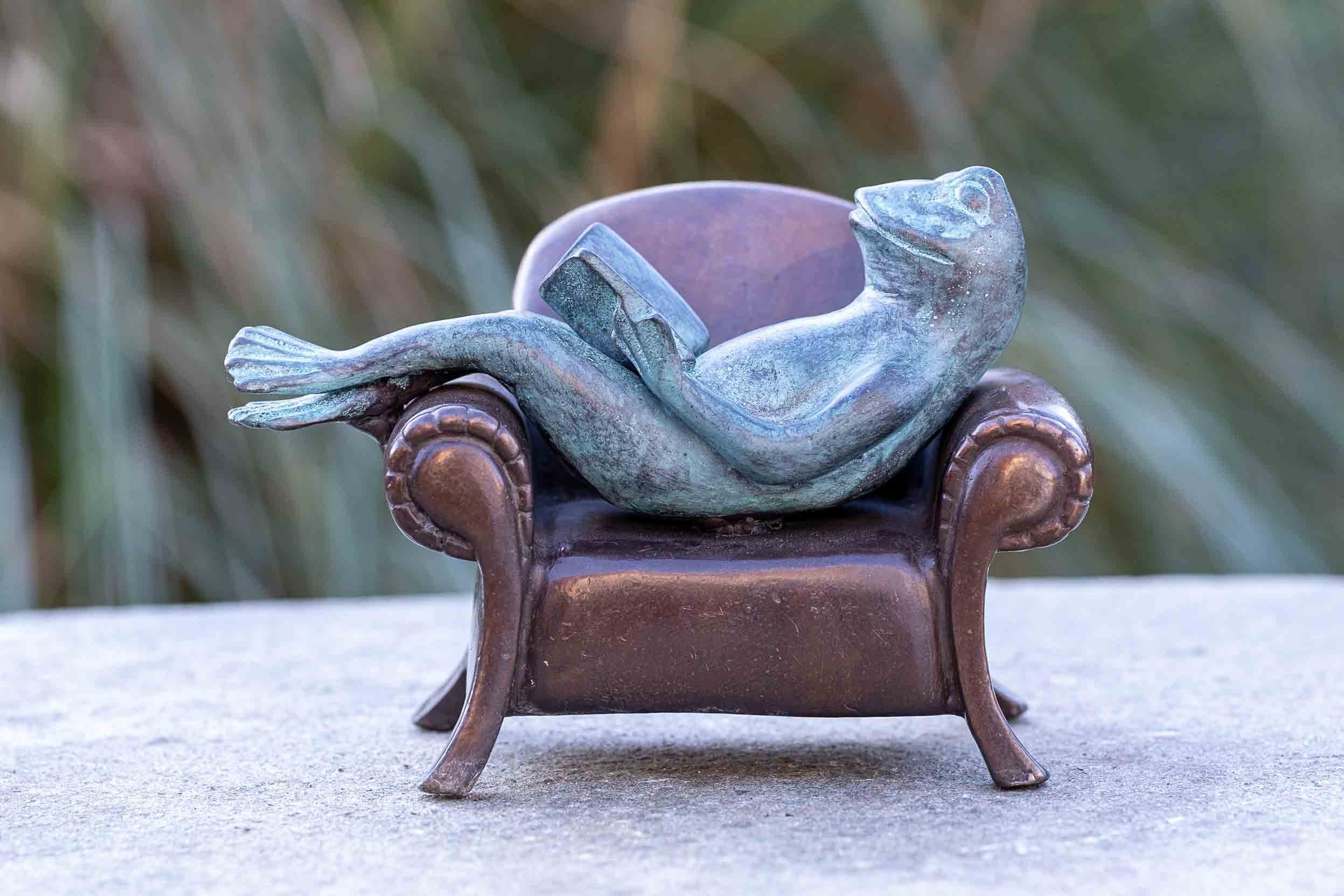 IDYL Dekofigur IDYL Bronze-Skulptur von gegen Frost, Bronze und Modelle auf Sofa, – Langlebig Bronze sehr in Die Lesender robust Frosch – gegossen einem witterungsbeständig patiniert. – in Wachsausschmelzverfahren werden und Regen Hand UV-Strahlung