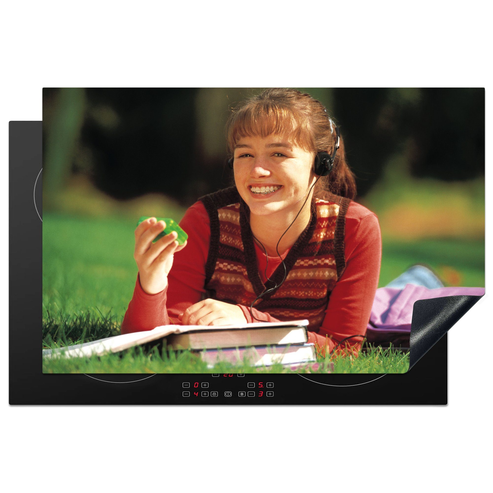MuchoWow Herdblende-/Abdeckplatte Ein im Gras liegendes Mädchen mit einem Buzzer in den 90er Jahren, Vinyl, (1 tlg), 81x52 cm, Induktionskochfeld Schutz für die küche, Ceranfeldabdeckung