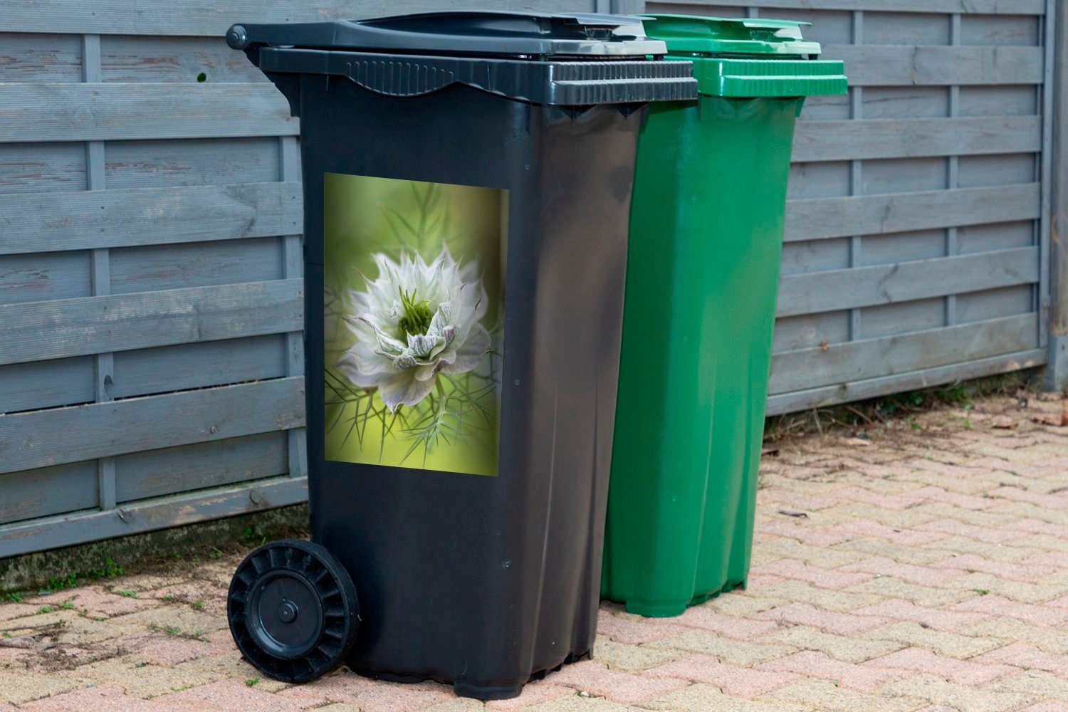 MuchoWow Wandsticker Eine Nigelblüte vor Container, grünem Abfalbehälter Mülleimer-aufkleber, (1 Sticker, Hintergrund St), Mülltonne