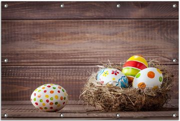 Wallario Sichtschutzzaunmatten Bunte bemalte Eier an Ostern im Vorgelnest vor hölzerner Wand