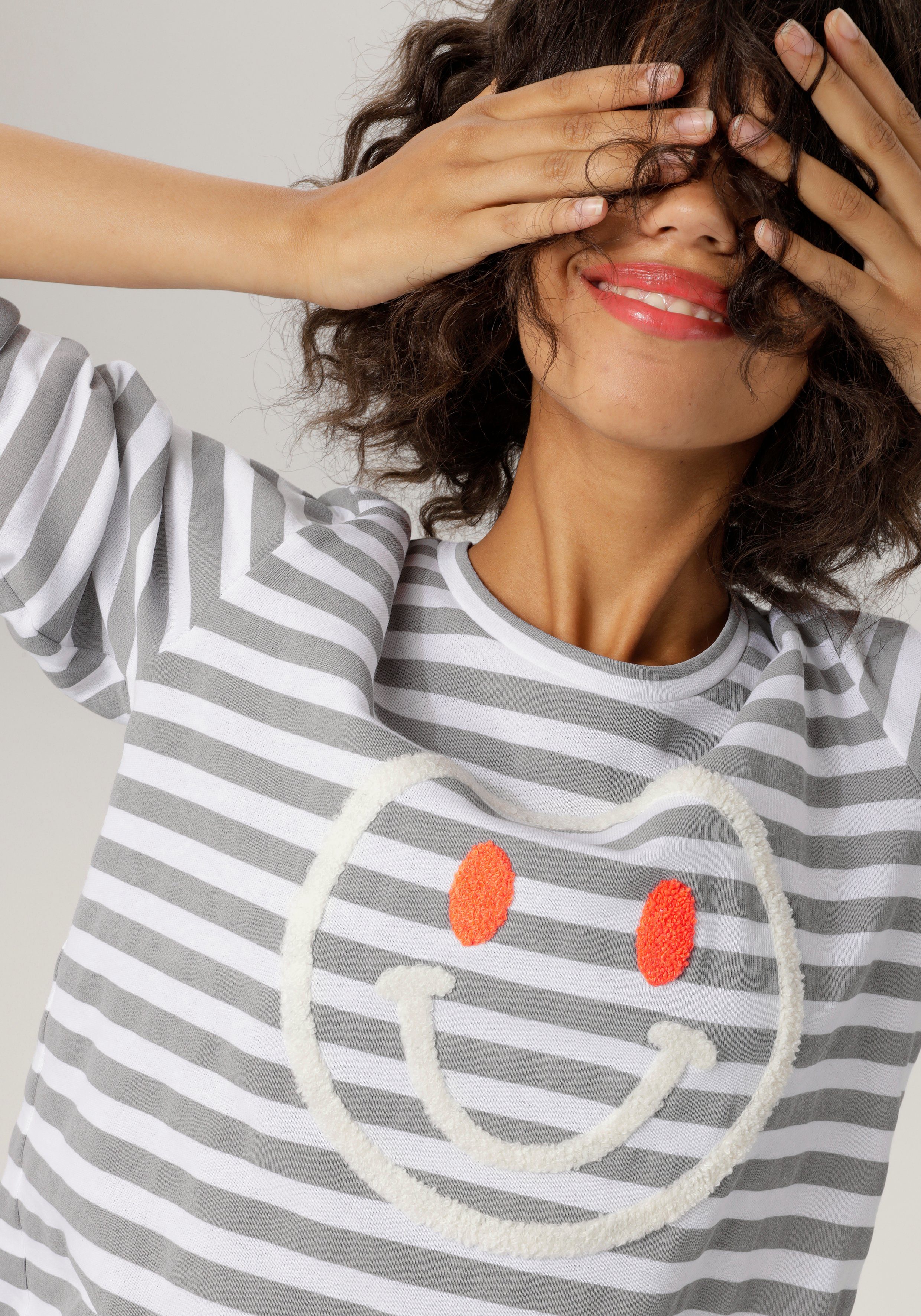CASUAL Sweatshirt Aniston hellgrau-weiß-wollweiß-orange fröhlicher Smiley-Applikation mit