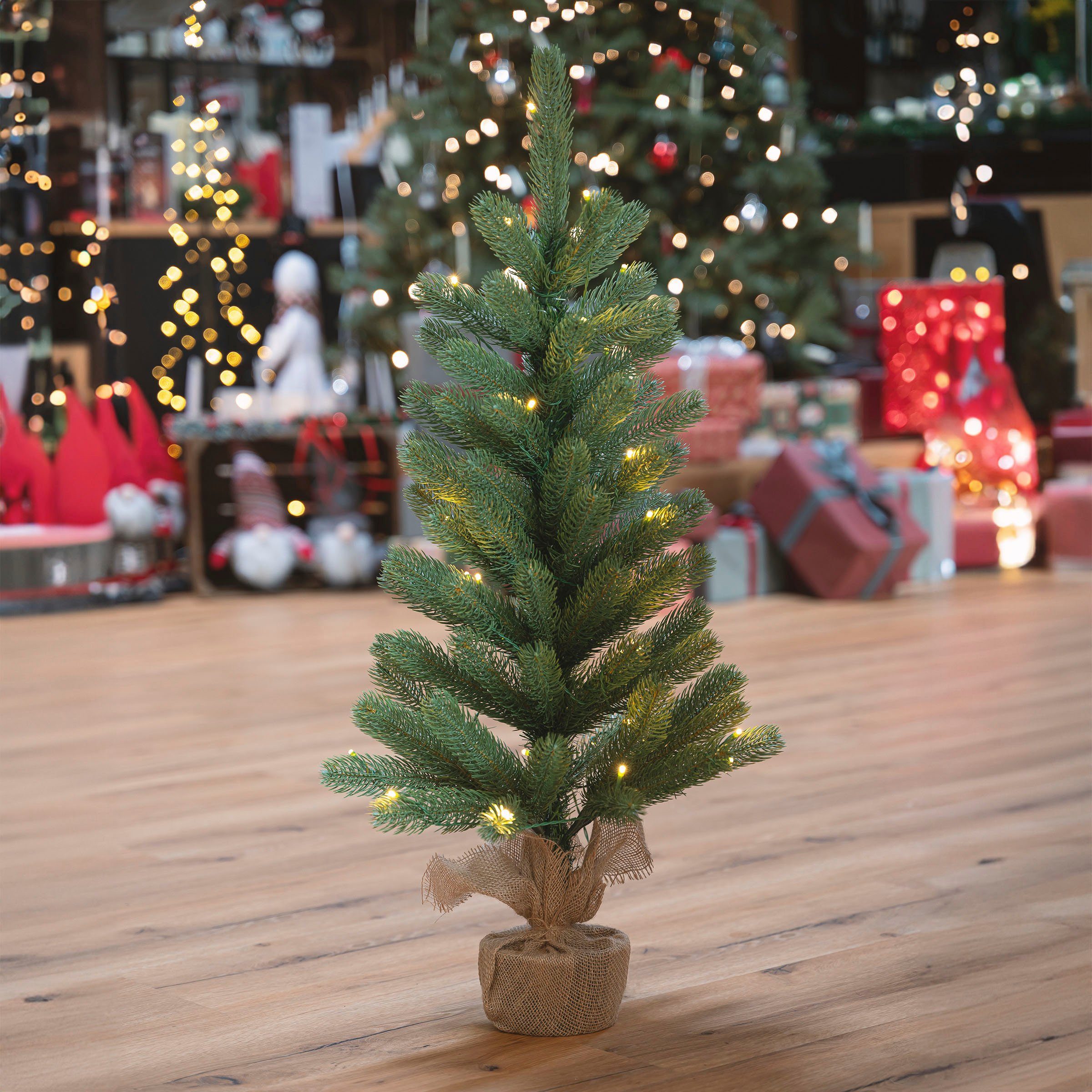 IC Winterworld Künstlicher Weihnachtsbaum LED-Tannenbaum, künstlicher Christbaum, Nordmanntanne, Weihnachtsdeko mit Jutebeutel um den Betonfuß, Batteriebetrieb
