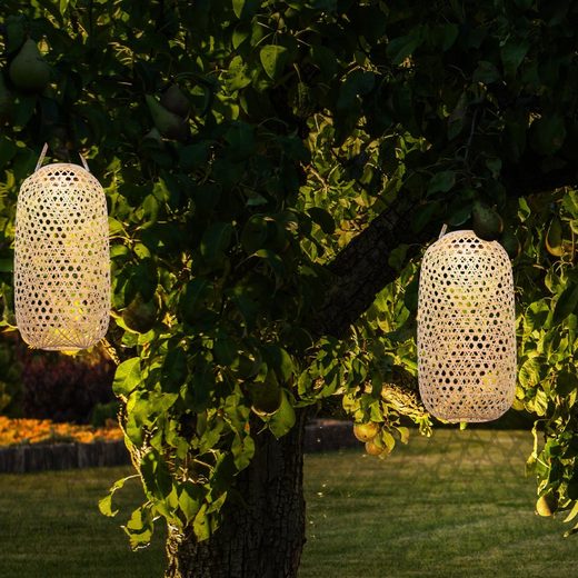 Die moderne Solar Hängeleuchte aus Bambus hängt in zweifacher Ausführung am Baum und bringt Licht in die Dunkelheit