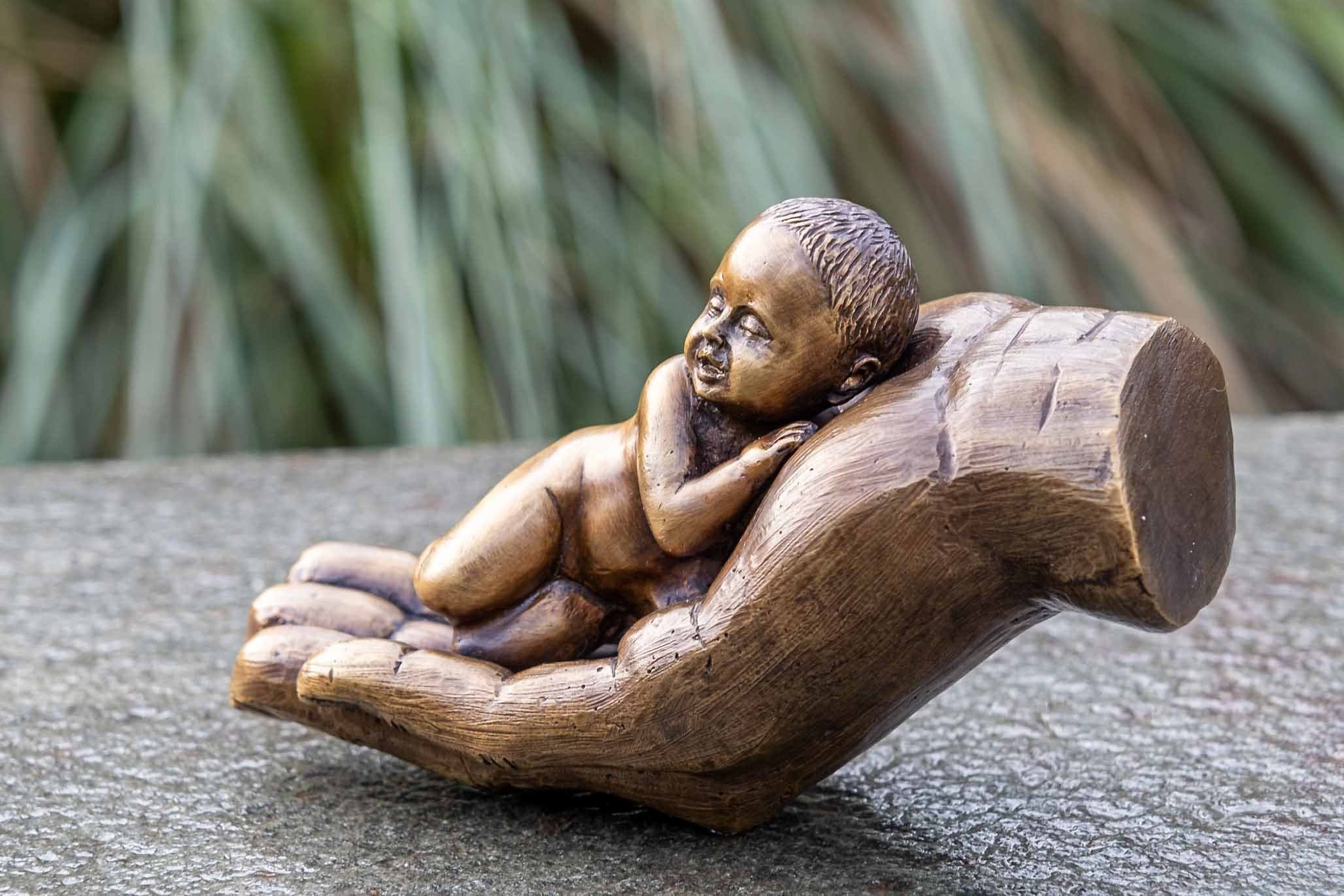 witterungsbeständig Langlebig – und – mit Gartenfigur Wachsausschmelzverfahren Bronze-Skulptur IDYL UV-Strahlung. einem Hand Hand Die Modelle werden in IDYL Baby, Eine und Bronze in von Frost, – sehr patiniert. robust Bronze gegen gegossen Regen