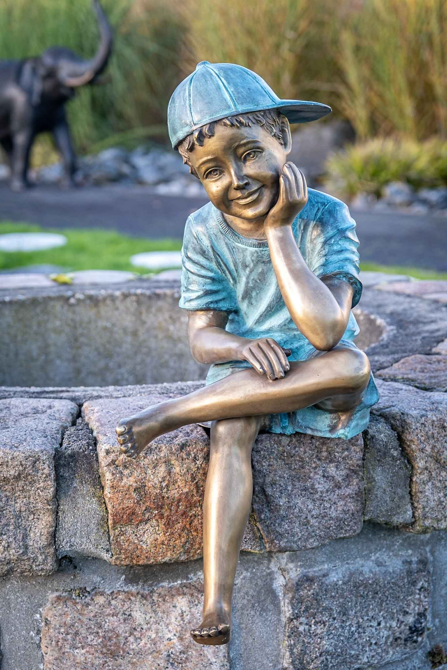 IDYL Gartenfigur IDYL Bronze-Skulptur Sitzender Junge mit einer Kappe, Bronze – sehr robust – Langlebig – witterungsbeständig gegen Frost, Regen und UV-Strahlung. Die Modelle werden in Wachsausschmelzverfahren in Bronze gegossen und von Hand patiniert.
