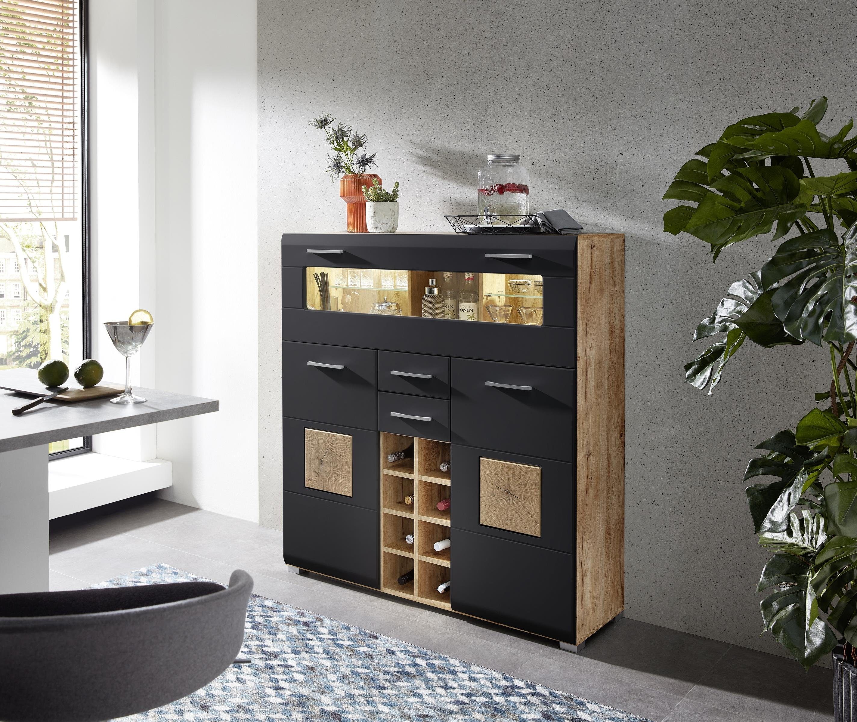 möbelando Barschrank "Sidonia I" Moderner Bartisch. Dekor - Korpus in Eiche Altholz Nachbildung, Fronten in Lack Laminat schwarz supermatt, MDF Perfect Touch, Absetzung Hirnholz Nachbildung, Griffe in Metall Chromfarbig matt mit 1 Flascheneintilung für 8 Flaschen, 1 Klappe mit Glaseinsatz, 2 Holztüren, 2 Schubkästen, 2 Glasböden und 4 Einlegeböden, inkl. LED-Beleuchtung. Breite 120 cm, Höhe 128 cm, Tiefe 37 cm.